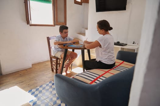 A mother and her young son engage in homework at a round table in a cozy home setting, fostering learning and togetherness.