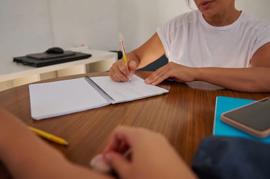 Two individuals are engaged in a writing task at a wooden table, focused on taking notes. This image conveys collaboration, education, and productivity.