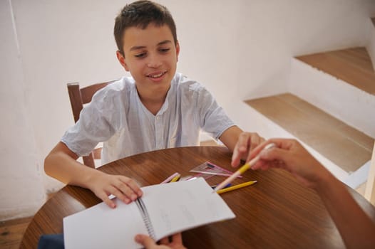 A young boy smiles while working on an educational task at a wooden table, engaging creatively with stationery.