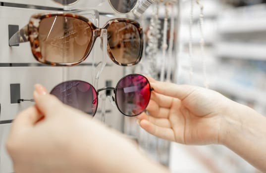 Young Girl In Store Choosing Glasses, Close-Up Shot Of Hands