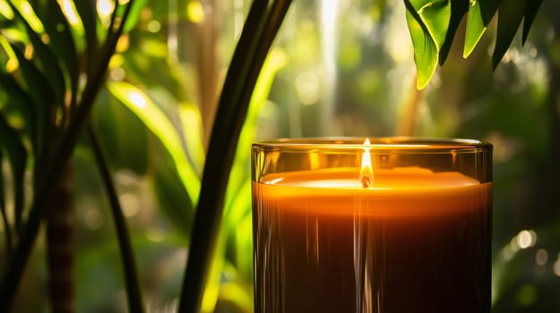 Close-up of a burning amber candle in a glass jar, with green leaves in the background, creating a relaxing and tranquil atmosphere