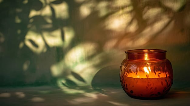 Amber candle burning in a glass jar, with botanical shadows cast on the wall behind it