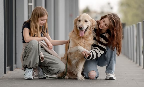 Two Girls With Golden Retriever Sitting And Playing Outside In Spring