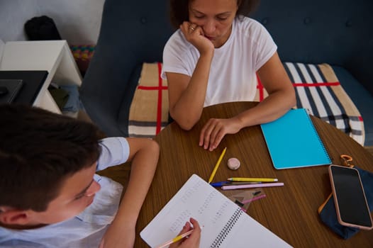 A mother helps her son with homework around a wooden table, fostering concentration and learning in a cozy home environment.