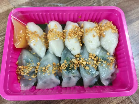 A plate of Choipan cakes from Indonesia sits on a wooden table. The cakes are white with green accents and are topped with a red sauce. Chopsticks are placed on the plate.