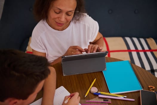 A woman and child engaging in learning with a tablet, notepads, and stationery on a wooden table, encouraging a shared educational experience in a cozy setting.