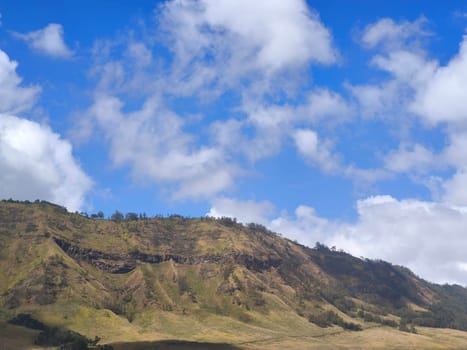 A picturesque landscape of rolling hills with vibrant green grass under a dramatic blue sky and fluffy white clouds.