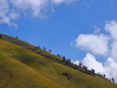 A picturesque landscape of rolling hills with vibrant green grass under a dramatic blue sky and fluffy white clouds.