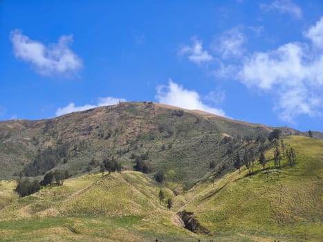 A picturesque landscape of rolling hills with vibrant green grass under a dramatic blue sky and fluffy white clouds.
