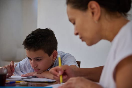 A mother and son focus intently on homework together at a dining table. The scene captures a moment of concentration and educational bonding, highlighting family support in learning.