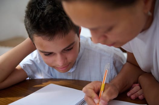 A caring mother assists her son with schoolwork at the kitchen table, fostering concentration and support.