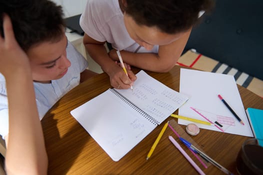 A mother assists her son with homework, focusing on mathematics. They sit at a kitchen table with notebooks and pens, sharing a moment of learning and encouragement.
