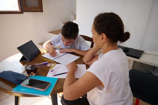 A mother supports her child with homework at a round table, emphasizing education, guidance, and family bonding in a warm home setting.