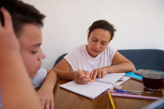 A dedicated teacher assists a student with homework in a cozy home setting, fostering learning with patience and care. Books, notebooks, and pencils are spread across the table.