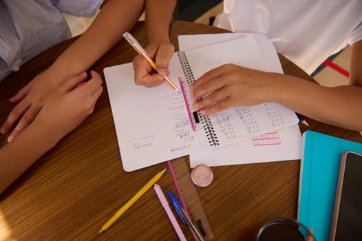 Close-up of students working together on math problems in a notebook. Cooperative learning, teamwork, and problem-solving are emphasized in this study session.
