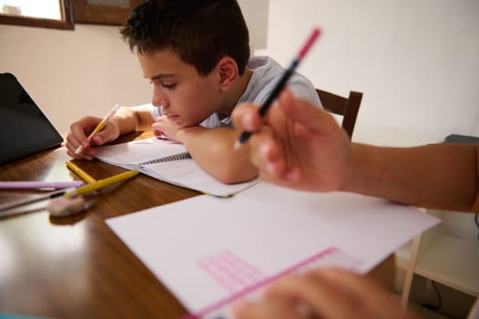 A young boy concentrates on his homework at a wooden table, surrounded by school supplies and a digital tablet, emphasizing focus and education.
