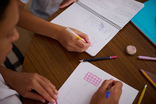 Top view of students working together on math homework, using pencils and graph paper. Collaboration and education concept.