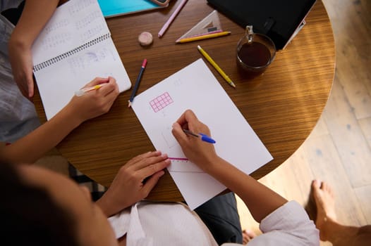 Top view of two students working on homework at a round table, with notebooks, pencils, and coffee. Collaborative learning setting.