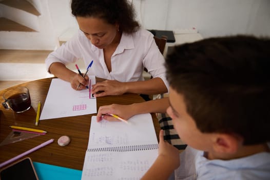 A mother and son collaborate on math homework at the kitchen table, fostering learning and communication. Pencils, paper, and focus are evident, emphasizing education and family bonding.