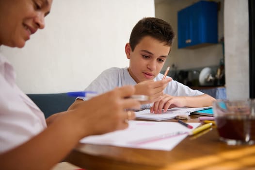 A mother and son sitting at a table, deeply engaged in a learning activity. The son is focused on a pencil and paper, exploring educational concepts. A warm family moment indoors.