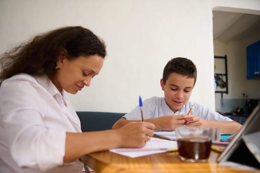 A mother and son sit at a table, deeply focused on their study materials. The atmosphere is encouraging and supportive, fostering learning and bonding.