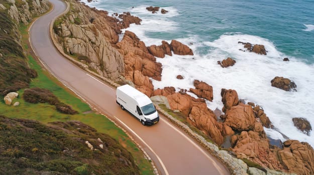 Aerial view of a white delivery van driving on a winding coastal road with a beautiful ocean view