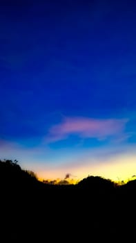 A picturesque silhouette of a landscape set against a vibrant sunset sky, showcasing a blend of blue, orange, and yellow hues. Perfect for themes of nature, tranquility, and beauty.