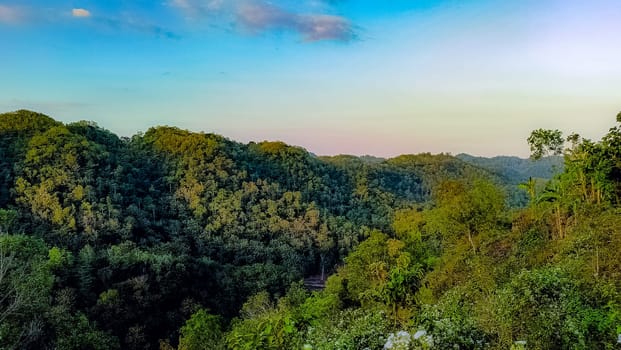 A tranquil mountain valley with lush greenery and a beautiful sunrise. The early morning light casts soft pastel colors over the landscape, creating a serene and peaceful ambiance.