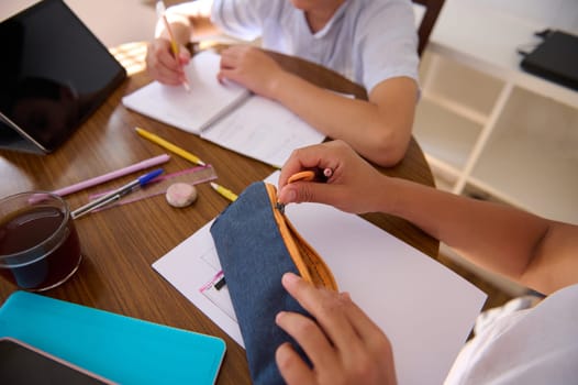 Two children study together, focusing on writing and drawing. The image conveys teamwork, learning, and concentration at a wooden table equipped with school supplies and a digital tablet.