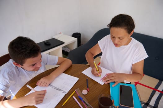 A mother and son sitting together at a table engaged in a learning session. The setting is relaxed, with notebooks and pens in use, showcasing the bond of family education.