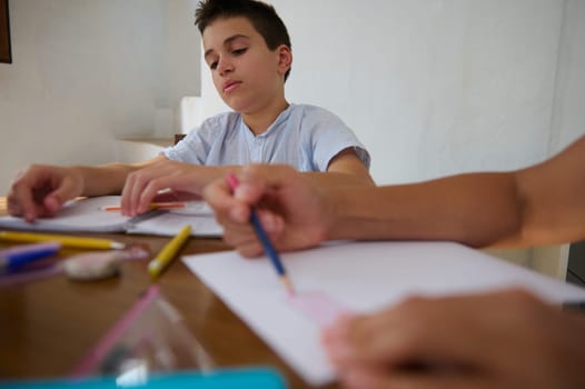 A young boy is intently working on his school homework, surrounded by colored pencils and paper. The setting is calm, depicting concentration and learning in a home environment.