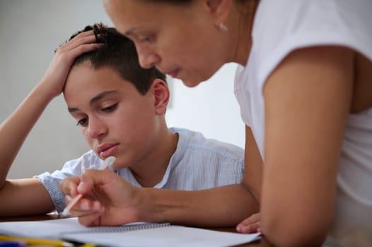 A mother assists her son with homework at home, emphasizing the importance of education. The young boy looks focused and determined as he engages in study with parental support.