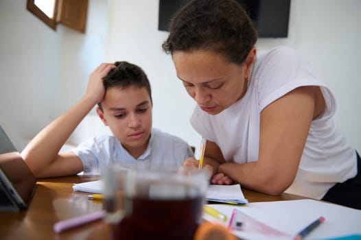 A mother assists her son with homework, providing guidance and support at the kitchen table, fostering education and learning in a cozy home environment.