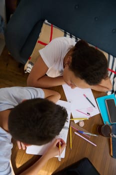 Overhead view of two students working together at a table with notebooks and pens, fostering collaboration and concentration in a cozy study environment.