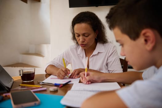 A mother and her son are focused on studying together at home, surrounded by study materials. Their teamwork reflects a supportive and educational environment.