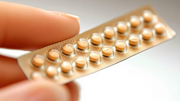 Woman is holding a blister pack of contraceptive pills between her fingers
