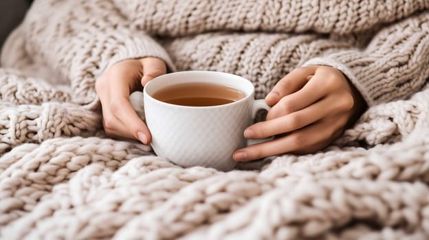 Woman relaxing on a sofa, enjoying a cup of hot tea under a warm blanket