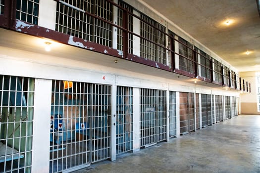 A desolate prison corridor with multiple metal cell doors, showcasing the aged structure. The dim lighting adds to the eerie ambiance, emphasizing themes of confinement and solitude.