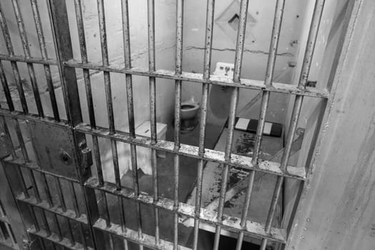 Explore a stark and isolated prison cell interior in black and white. This image evokes feelings of solitude, confinement, and the harsh realities of incarceration.
