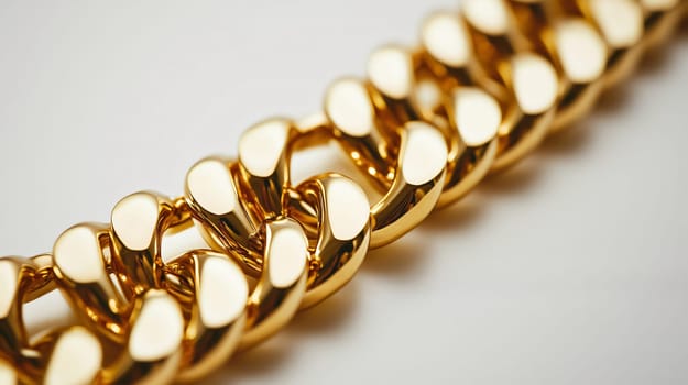 Thick gold chain is laying flat on a white surface, catching the light and gleaming