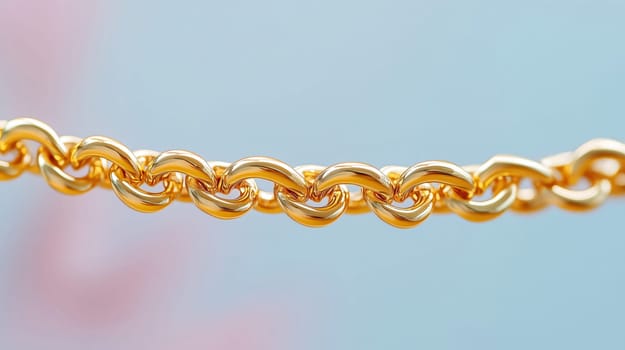 Shiny gold chain is hanging in front of a pastel blue and pink background