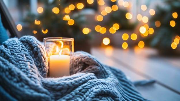 Burning candle is resting on a knitted blanket with bokeh lights in the background, creating a warm and cozy atmosphere