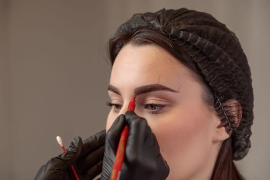 Beautician preparing a woman for microblading treatment, drawing eyebrow shape on her face