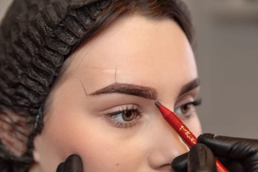 Beautician applying eyebrow makeup to young woman in beauty salon