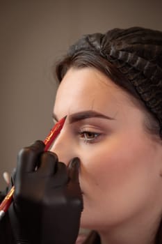 Beautician preparing eyebrows for permanent makeup by drawing lines with red pencil
