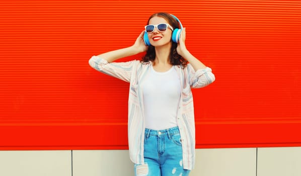 Portrait of happy smiling young woman with headphones listening to music on red background
