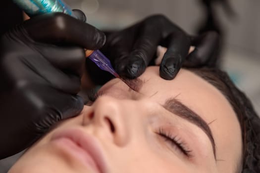 Beautician performing microblading procedure on eyebrows of client in beauty salon