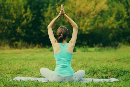 Young woman doing yoga exercises on a mat on the grass in summer park