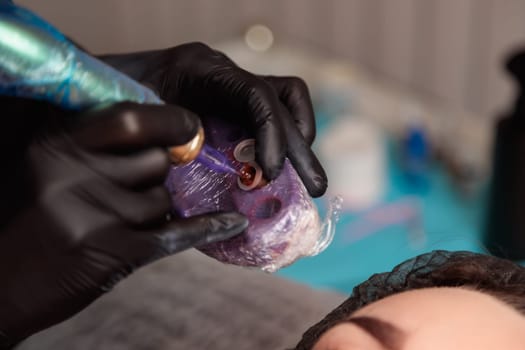 Beautician preparing to apply permanent makeup, picking up red pigment with a tattoo machine