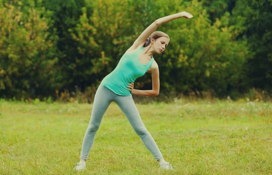 Fitness woman doing stretching exercises on the grass in summer park